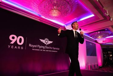 A man in a suit speaks on stage at the Royal Flying Doctor Service 90 years event.