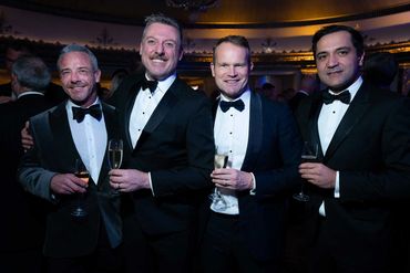 Four men in tuxedos holding glasses of champagne at a formal event.
