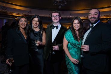 Five people dressed elegantly at a formal event holding champagne glasses.