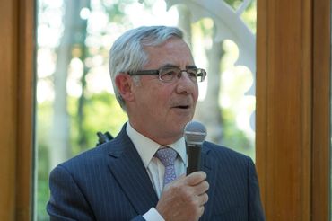 Older man in a suit speaking into a microphone indoors.