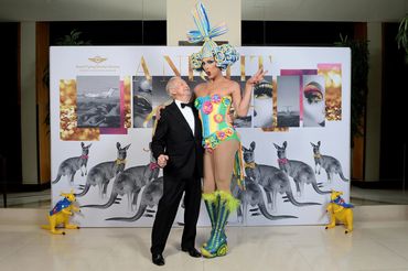 A man in a tuxedo and a tall drag performer in a colorful costume pose together.