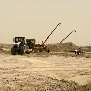 Construction site with heavy machinery and workers in a sandy desert.