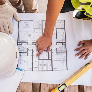 Construction workers reviewing a building blueprint on a wooden surface.