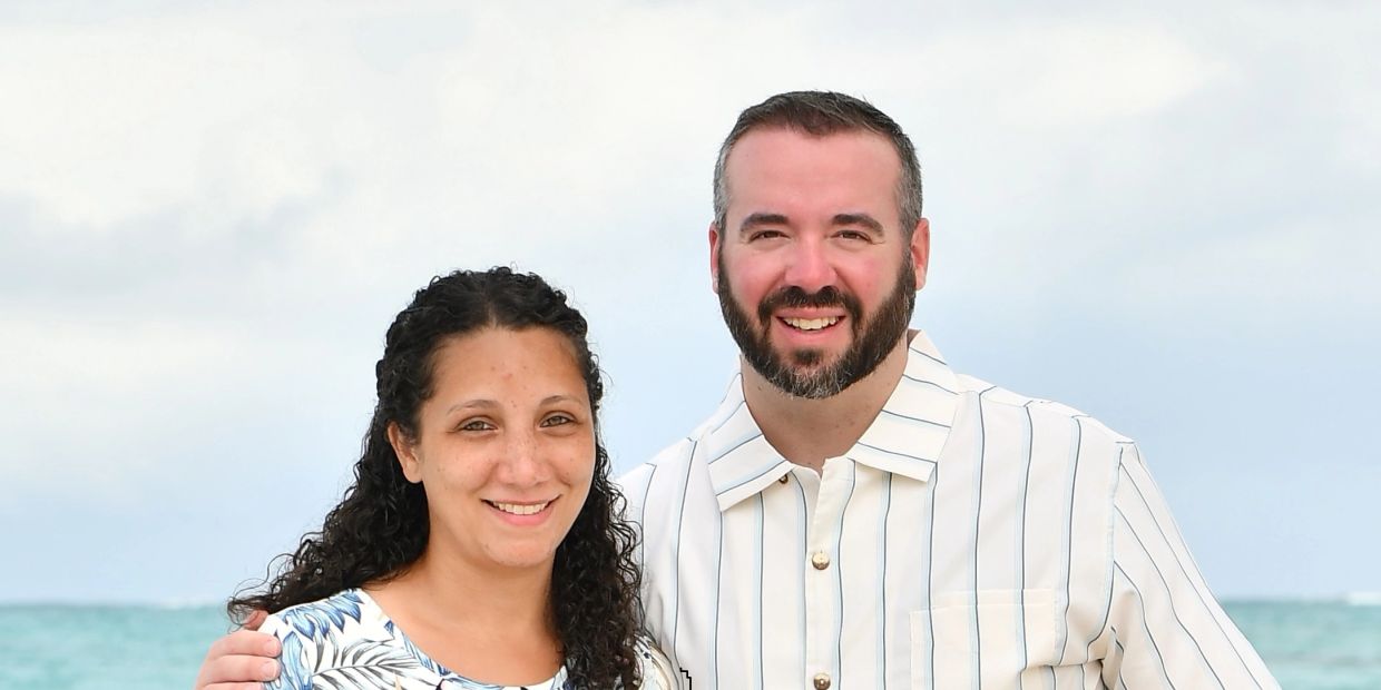 Smiling couple posing together by the ocean with a cloudy sky.