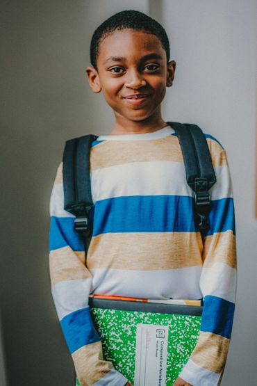 Smiling boy with backpack and notebook ready for school.