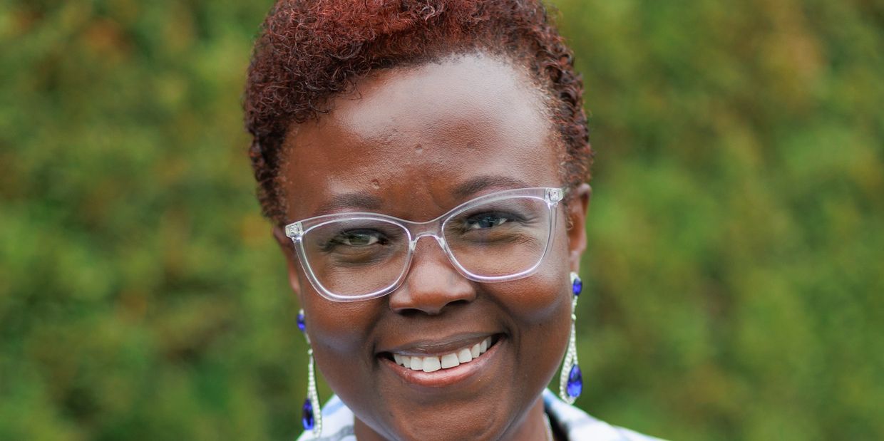 Smiling woman with clear glasses and blue earrings against a green background.