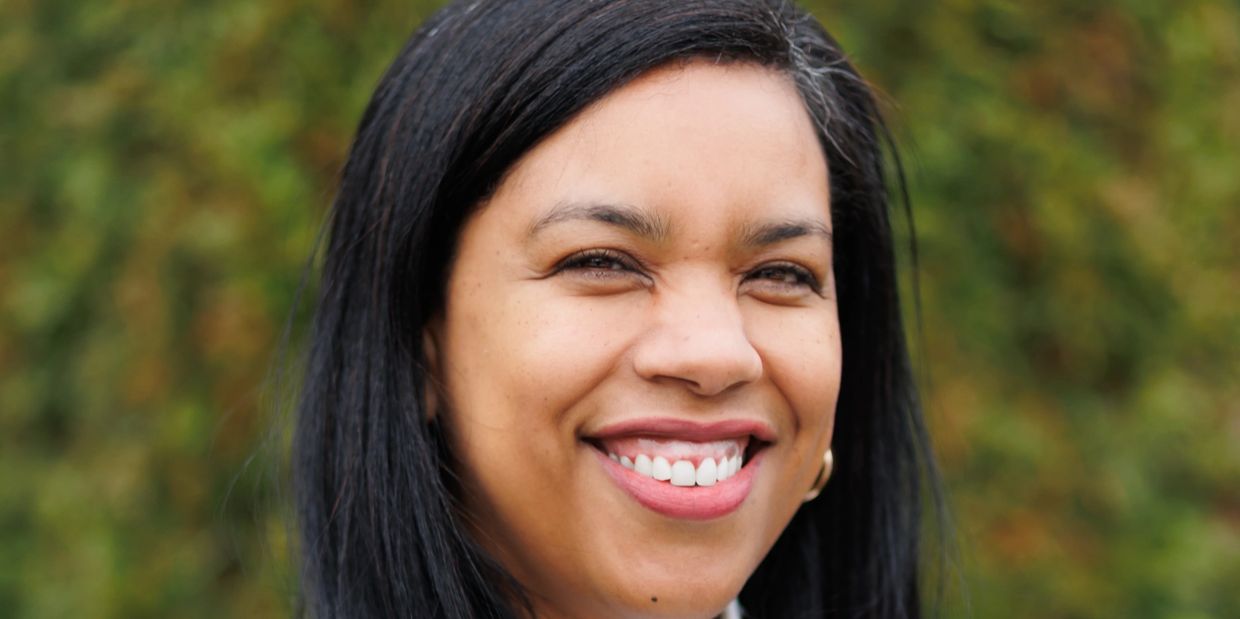 Close-up portrait of a smiling woman with long black hair and a blurred green background.