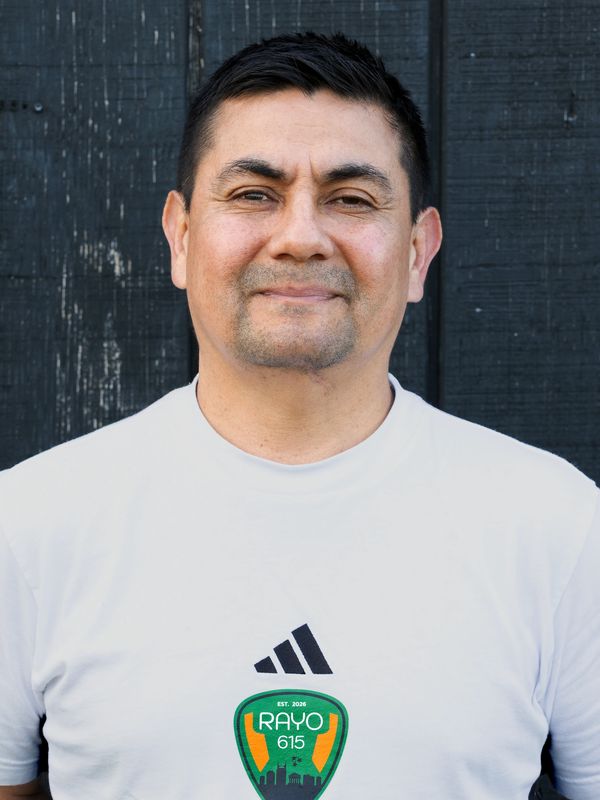 Man wearing a white Rayo 615 sports t-shirt smiles gently.