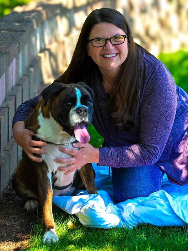 Woman smiling with her dog outdoors on the grass.