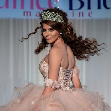 Woman in a sparkling gown and tiara spins gracefully on stage.