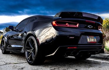 Sleek black Chevrolet Camaro SS with custom license plate under dramatic sky.