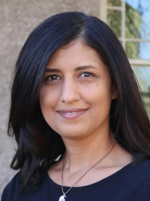 Smiling woman with long black hair and a pendant necklace.