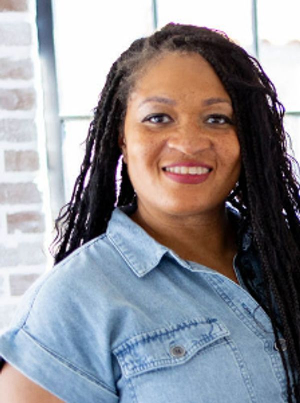 A smiling woman with long braided hair wearing a denim shirt.