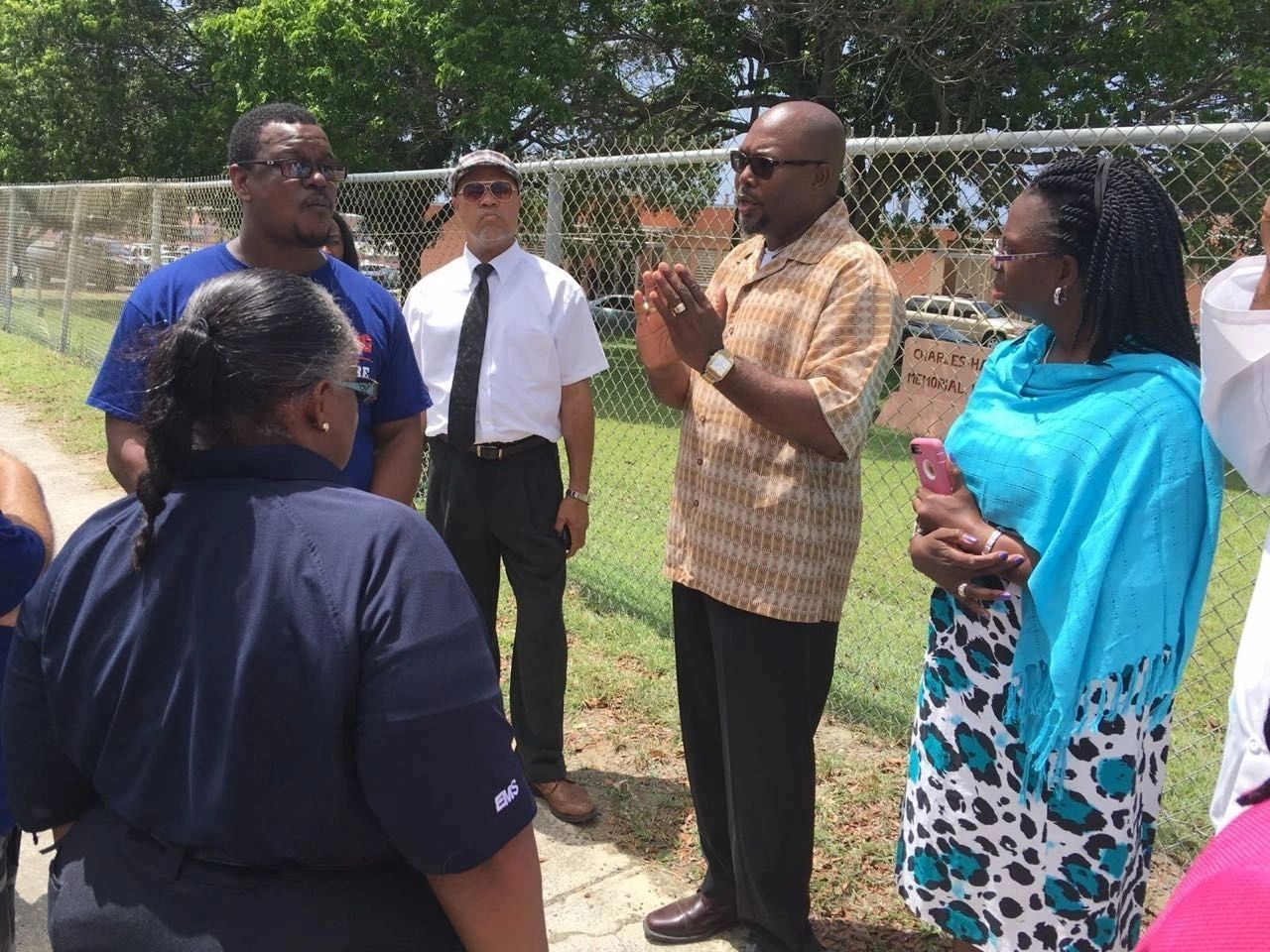 A group of people engaged in a serious outdoor discussion near a chain-link fence.