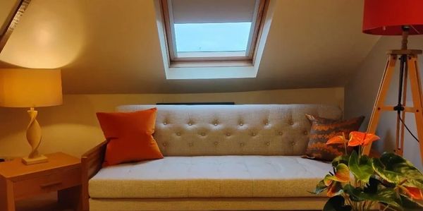 Warm therapy loft with a beige sofa, soft lighting, orange cushions and a plant. A calm, inviting space used for somatic therapy, grounding techniques and nervous system regulation.