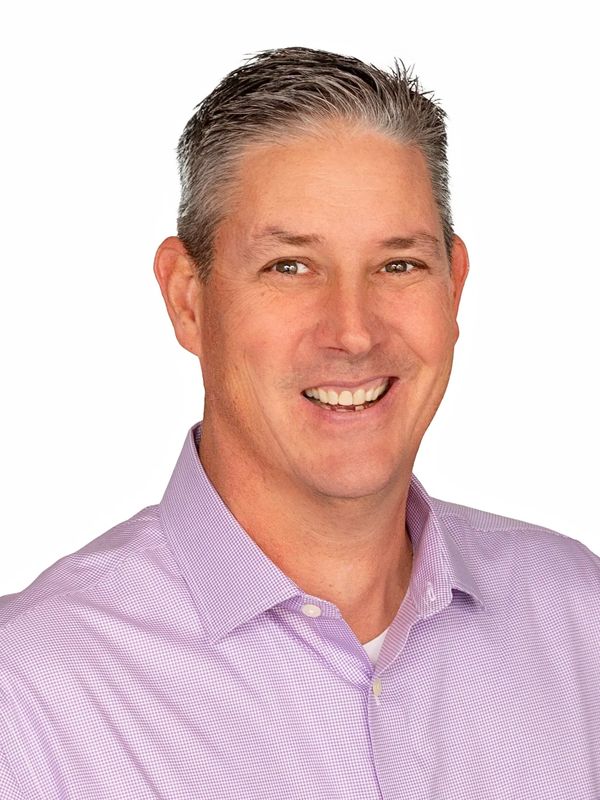 Smiling man in a light purple checkered shirt against a white background.