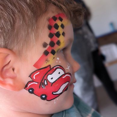 Child with a red race car face paint and checkered flag design.