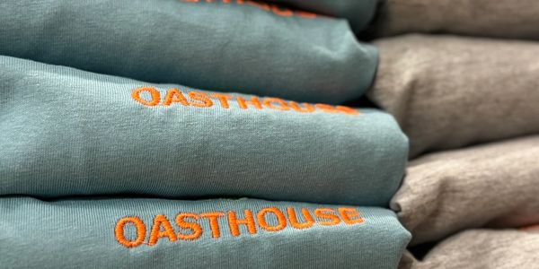 Neatly folded blue and gray sweatshirts with OASTHOUSE embroidered in orange.