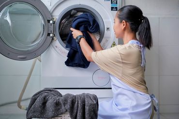 Woman loading clothes into a front-load washing machine in a laundry room.