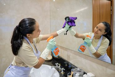 Woman cleaning a bathroom mirror with a spray bottle and cloth.