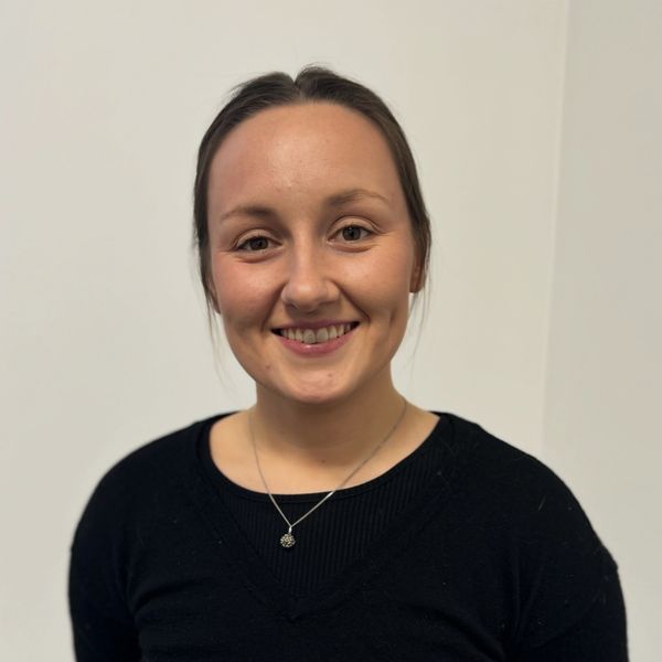 Smiling woman with dark hair in a black sweater against a plain background.