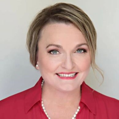 Professional woman smiling in a red blouse with pearl necklace.