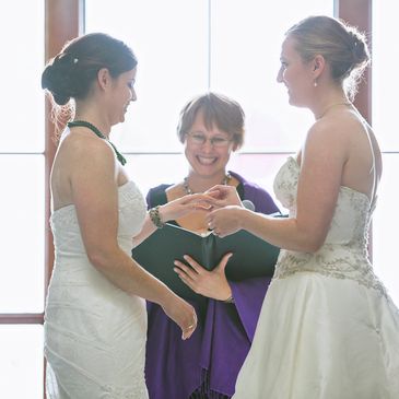 A photograph of two brides exchanging wedding rings.