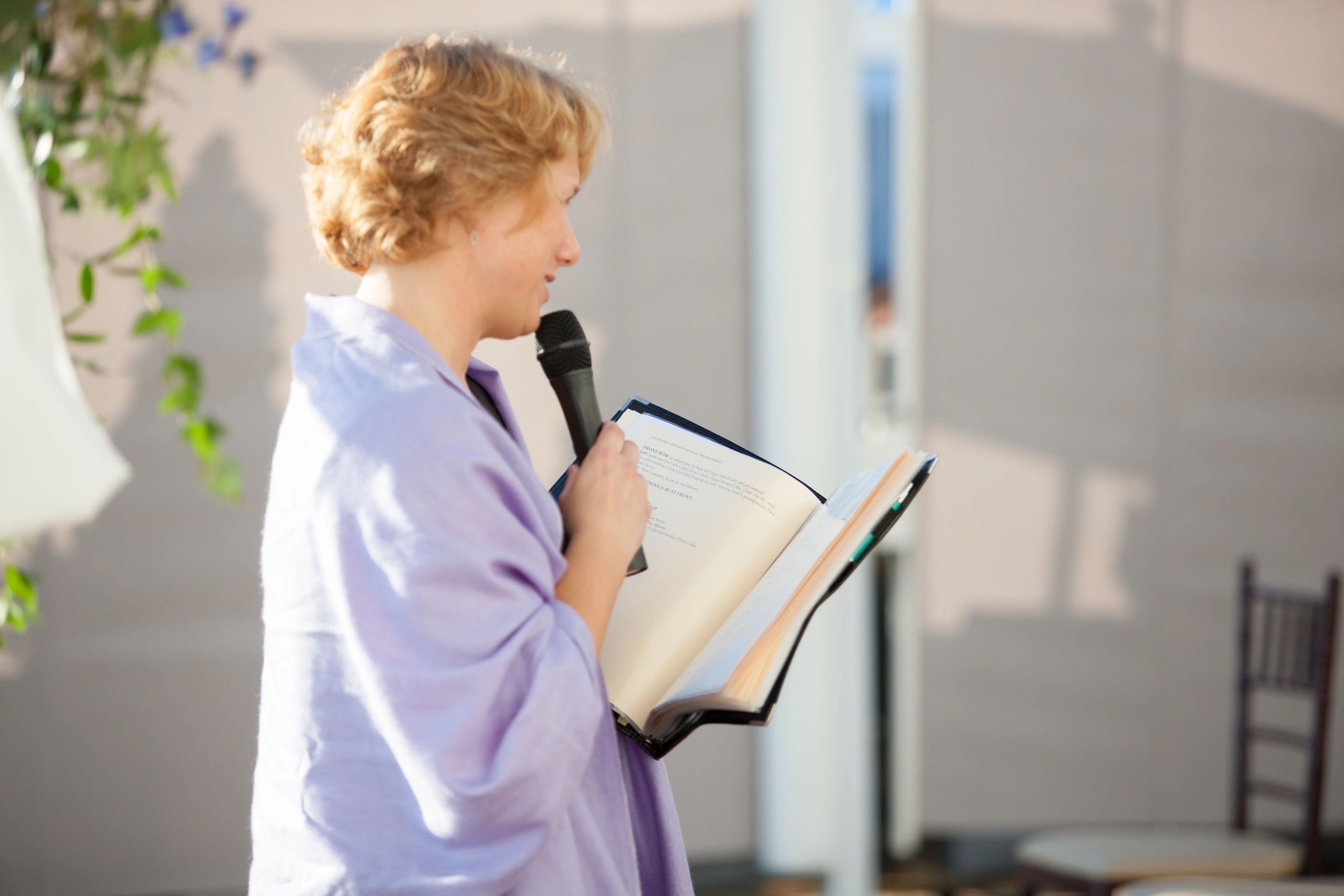 A photograph of an officiant reading from a binder, with a microphone.