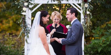 A photograph of a bride and a groom at a wedding, with an officiant.