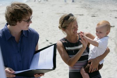 A photograph of a mother and son at a baby blessing, with an officiant.