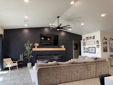 Modern living room with dark accent wall, large sectional sofa, and ceiling fan.
