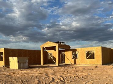 Wooden frame of a house under construction on a dirt lot.