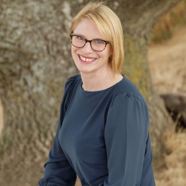 Smiling woman with glasses in front of a tree.