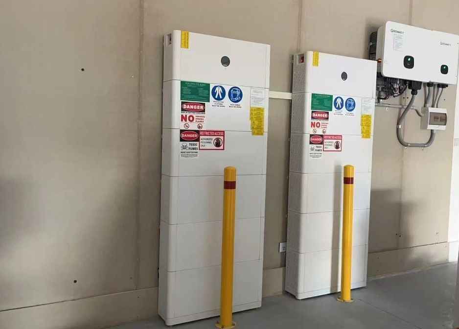 Two white electrical units with safety signs and yellow protective bollards inside a room.