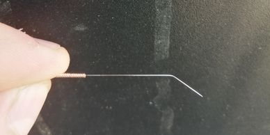 Hand holding a thin metal wire with a coiled end against a dark background.