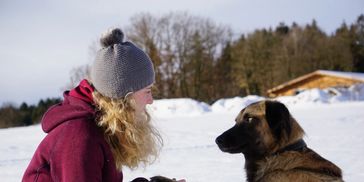 A person in winter clothing faces a dog in a snowy landscape.