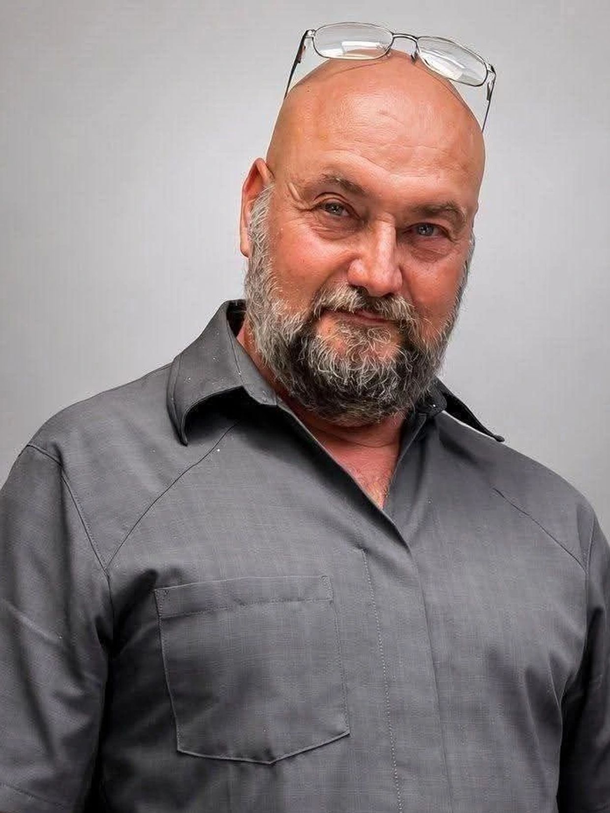 Bald man with beard wearing glasses on his head and gray shirt.
