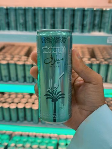 Hand holding a no-sugar-added cola can with dates extract in a store.