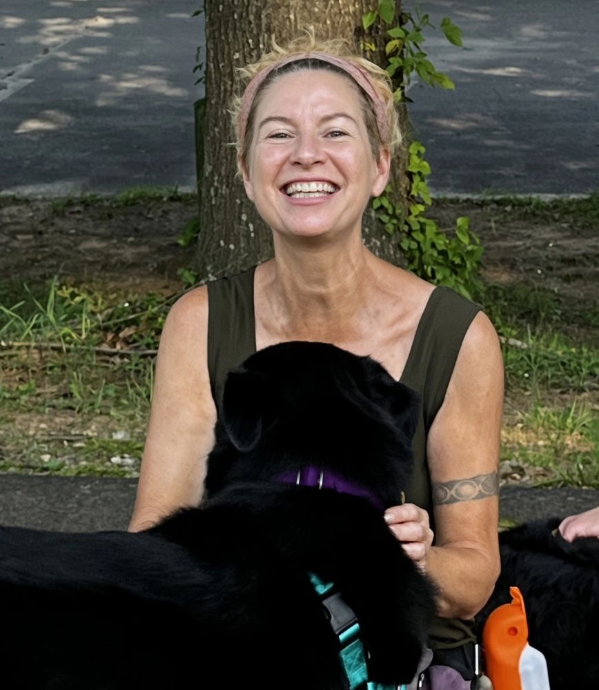 Smiling woman sitting outdoors with a black dog.