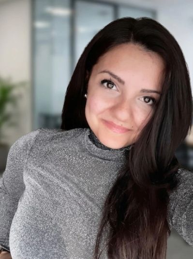 A young woman with long dark hair smiling warmly indoors.
