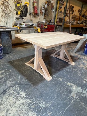 Handcrafted wooden table in a busy workshop with tools and equipment.