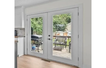 Glass double doors open to a backyard deck with outdoor furniture and a grill.