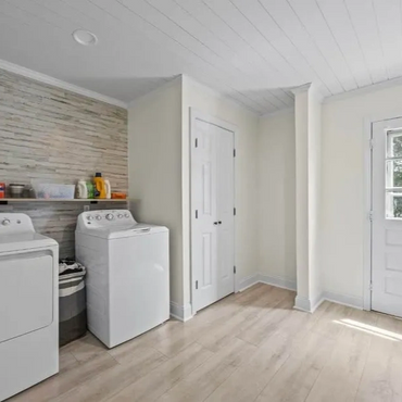 Bright laundry room with washer, dryer, and storage shelf.