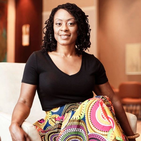 Confident woman sitting indoors wearing a black top and colorful skirt.