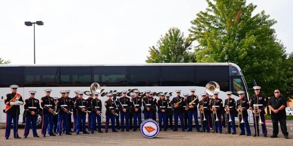 Marine band members posing with instruments in front of a bus.
