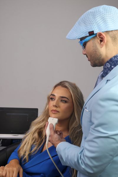 A doctor performs a facial ultrasound on a female patient in a clinical setting.