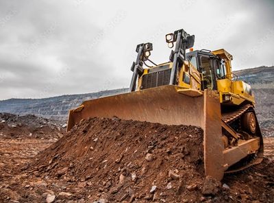 Yellow bulldozer pushing dirt at a construction site under a cloudy sky.