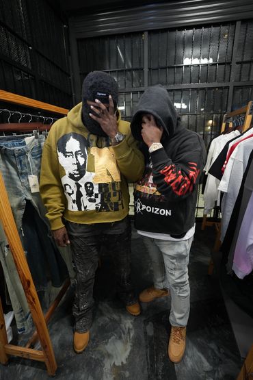 Two men in hoodies covering their faces in a clothing store.