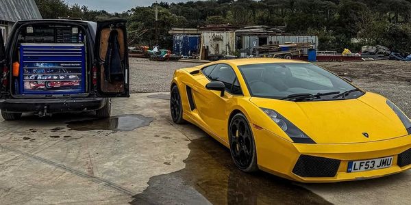 Yellow Lamborghini parked next to a black van with open doors in an industrial yard.