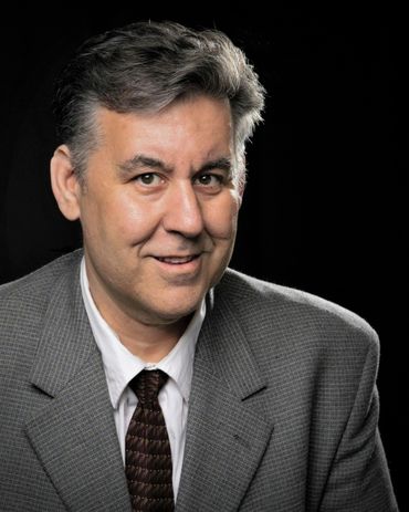 Middle-aged man in suit smiling against a black background.
